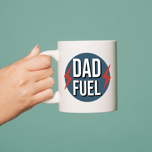 Hand holding a mug with 'Dad Fuel' design on a solid background